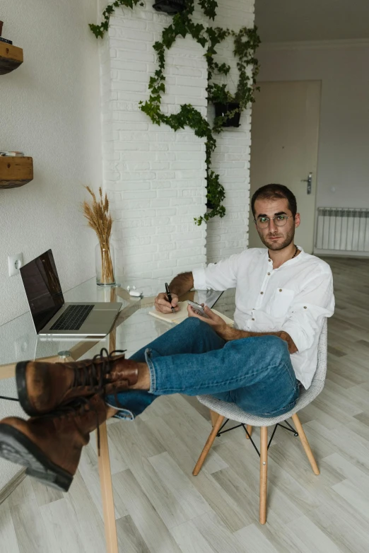 a man sitting at a table in front of a laptop, by Ivan Grohar, pexels contest winner, wearing boots, apartment, thin young male, edin durmisevic