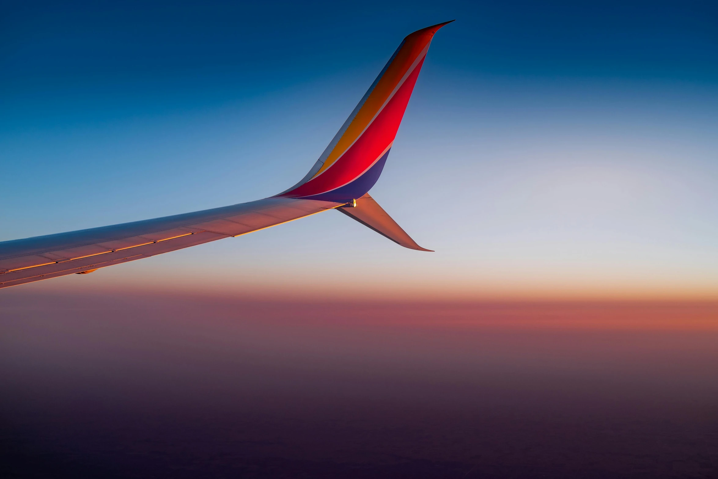 the wing of an airplane flying in the sky, by Matt Cavotta, pexels contest winner, minimalism, colorful sunset, tail fin, multicolored, resting