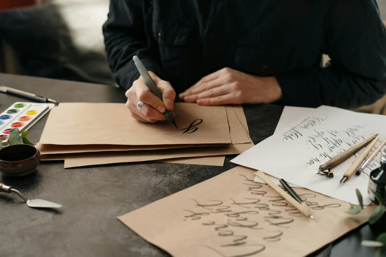 a person sitting at a table writing on a piece of paper, packaging design, brown paper, calligraphy, thumbnail