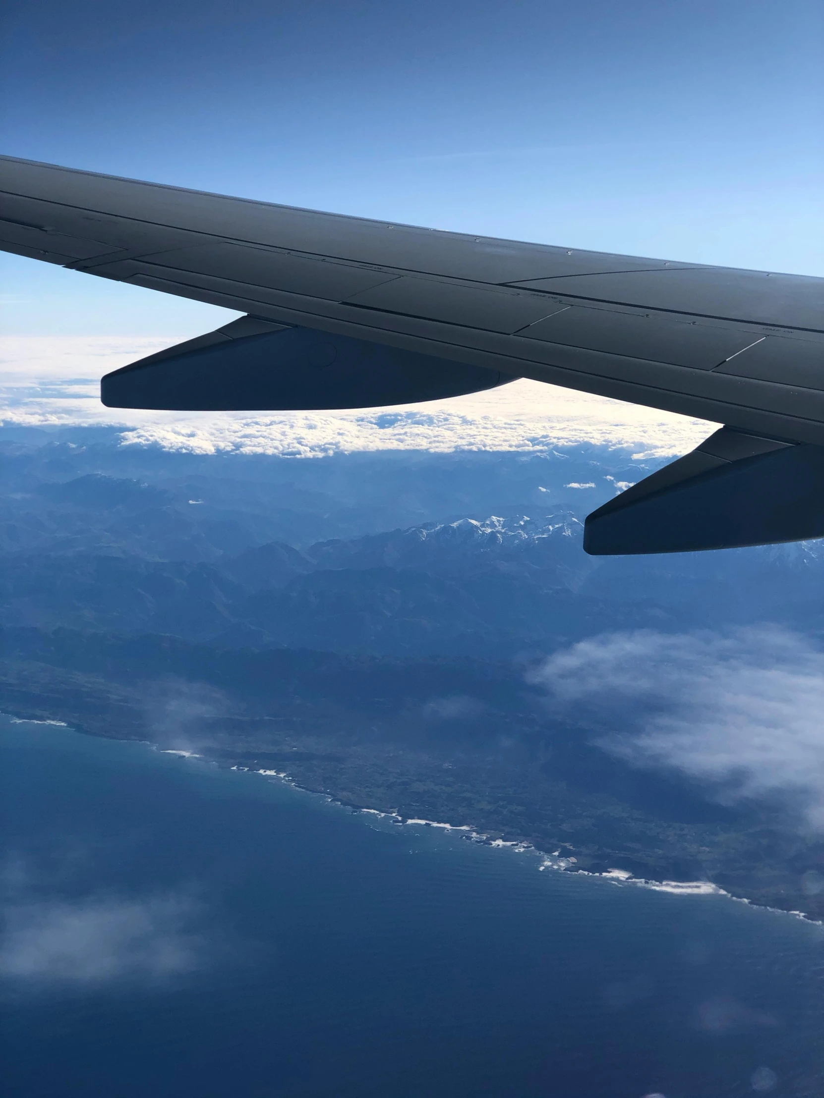 the wing of an airplane flying over a body of water, the alps are in the background, ocean view, insanly detailed, bay area