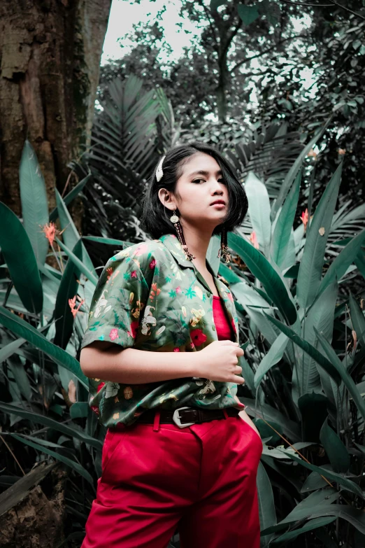 a woman standing in the middle of a lush green forest, an album cover, trending on pexels, sumatraism, red shirt, floral clothes, aggressive look, tropical style