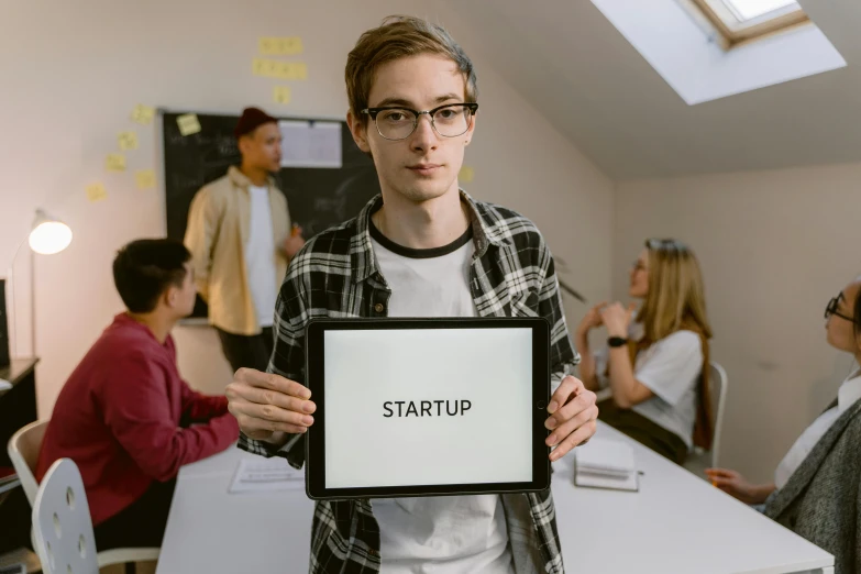a man holding a sign that says startup, a picture, trending on pexels, wearing square glasses, male teenager, center of image, holding notebook
