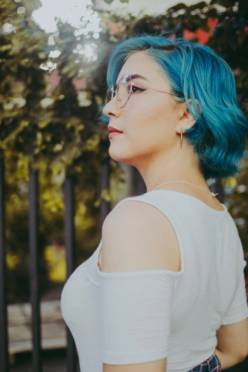 a woman with blue hair standing in front of a fence, inspired by Elsa Bleda, trending on pexels, wearing square glasses, looking across the shoulder, half body photo, hyperealistic photo