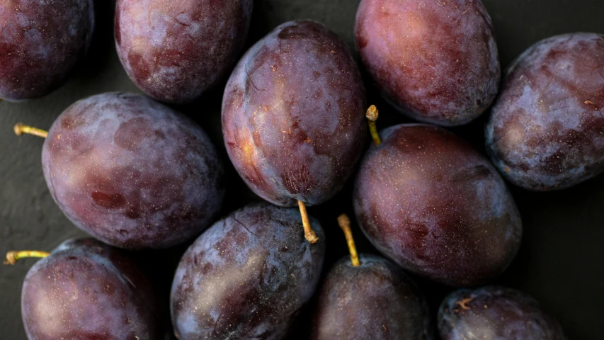 a pile of plums sitting on top of a table, zoomed out to show entire image, background image, dark purple, portrait image