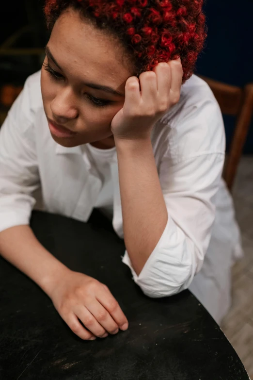 a little girl sitting at a table with her hand on her head, trending on unsplash, renaissance, young asian woman, wearing a white button up shirt, studious chiaroscuro, sad feeling