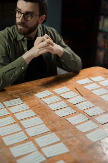a man sitting at a table with post it notes on it, an album cover, by Matthias Stom, unsplash, trade card game, in a workshop, labels, pair of keycards on table