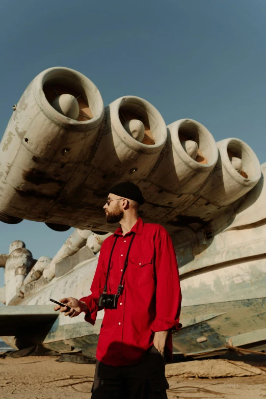 a man in a red shirt standing in front of a boat, an album cover, pexels contest winner, surrealism, monuments, rapper, giant guns, in barcelona