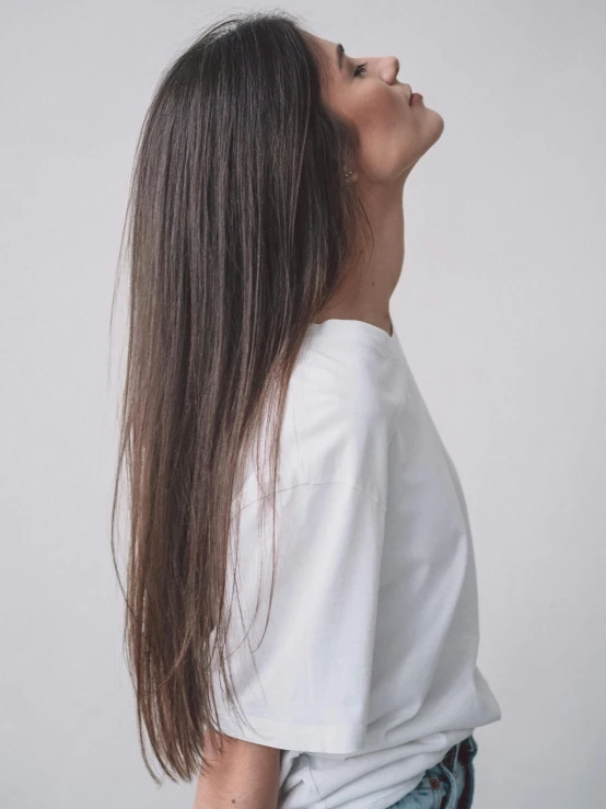 a woman with long hair standing in front of a white wall, trending on unsplash, wearing a white hospital gown, brown long and straight hair, view from the side, on a gray background