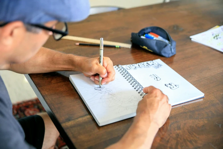 a man sitting at a table writing on a notebook, a drawing, 9 9 designs, traditional animation, mixed art, idealised