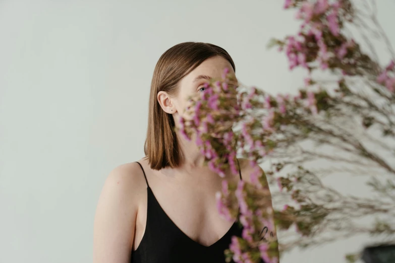 a woman standing in front of a vase of flowers, an album cover, pexels contest winner, smooth pale skin, she is wearing a black tank top, her face is a mauve flower, sydney sweeney