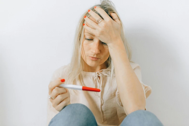 a woman sitting on the floor with a thermometer in her hand, trending on pexels, happening, showing forehead, red ballpoint pen, devastated, gif