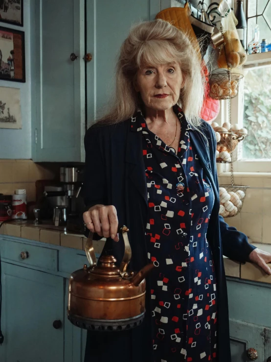 a woman standing in a kitchen holding a kettle, a portrait, by Penelope Beaton, journalism photo, portrait image