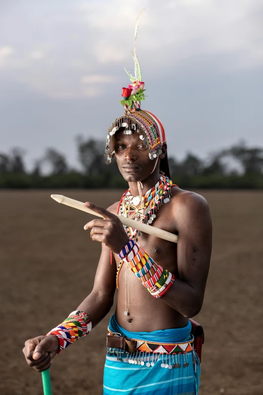 a man standing in a field holding a frisbee, an album cover, inspired by Afewerk Tekle, pexels contest winner, afrofuturism, tribal makeup, beads, holding scimitar made of bone, very kenyan