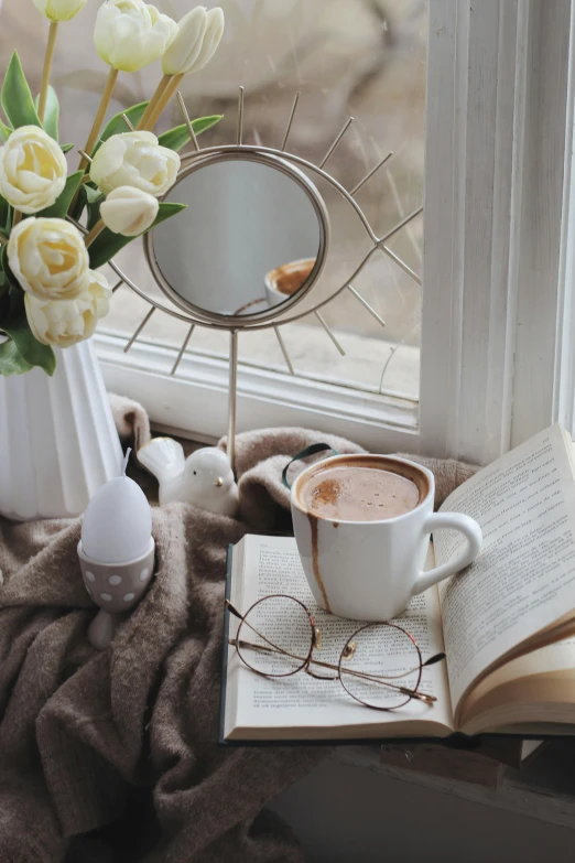 a cup of coffee and a book on a window sill, a still life, pexels contest winner, romanticism, round mirror on the wall, white reading glasses, silver egg cup, sitting on a mocha-colored table