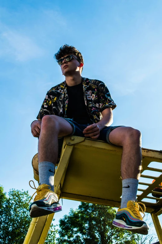 a man sitting on top of a yellow bench, by Jacob Toorenvliet, wearing shorts, dark shades, declan mckenna, patterned clothing