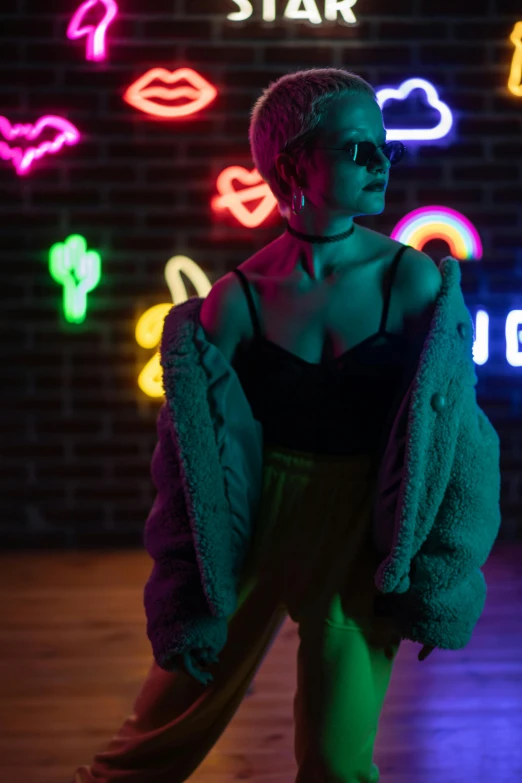 a woman standing in front of neon signs, trending on pexels, non binary model, cozy lights, coat for a rave, ((neon colors))