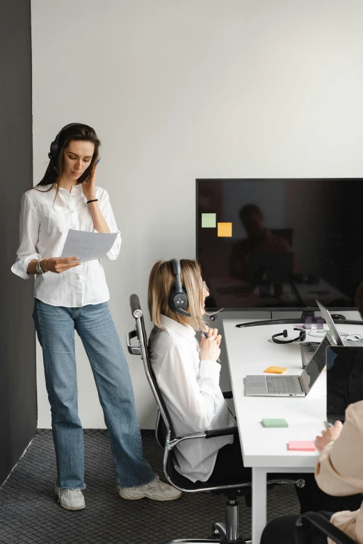 a woman standing in front of a desk talking on a cell phone, floating headsets, creative coding, coworkers, sitting in front of a microphone