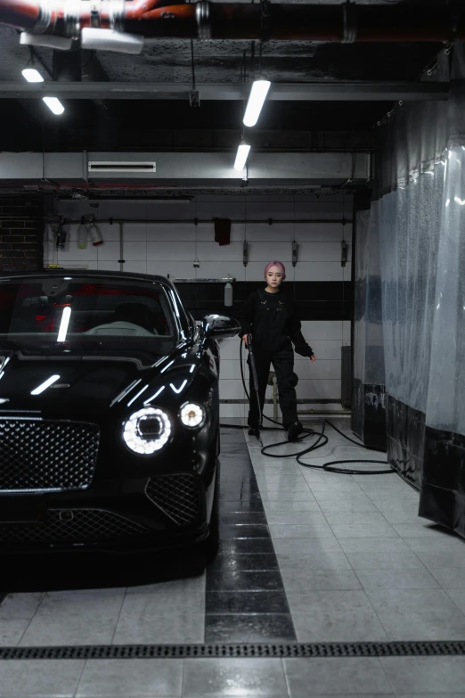 a man standing next to a black car in a garage, bentley, cinematics lighting, hoses, extremely clean