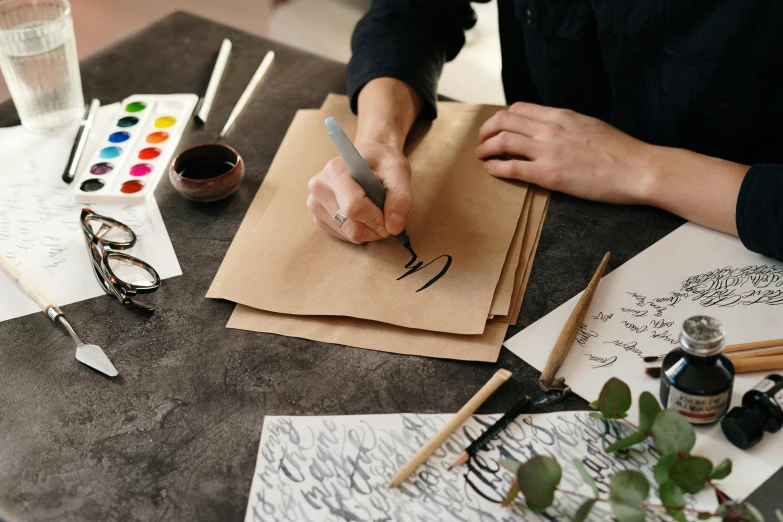 a person sitting at a table writing on a piece of paper, inspired by Masamitsu Ōta, trending on pexels, process art, brown paper, “modern calligraphy art, avatar image, paper decoration