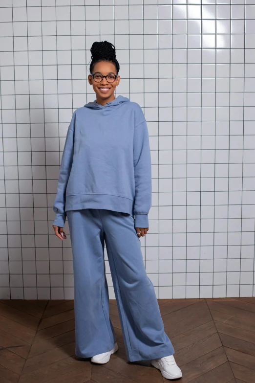 a woman standing in front of a tiled wall, inspired by Tadashige Ono, happening, wearing a hoodie and sweatpants, relaxed. blue background, tonal topstitching, very tall