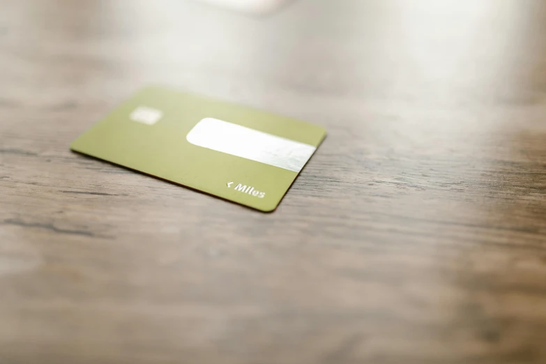 a green credit card sitting on top of a wooden table, by Julian Allen, private press, square, ochre, highkey, ambiance