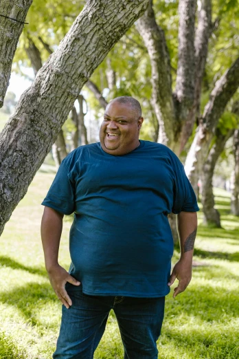 a man standing next to a tree in a park, happening, plus-sized, smiling, belly free, huell babineaux