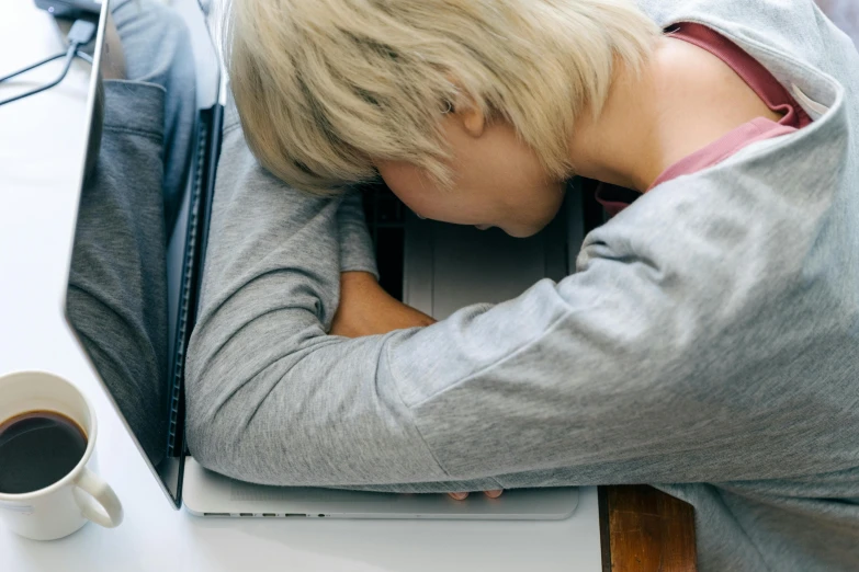 a woman sleeping on top of a laptop next to a cup of coffee, by Nina Hamnett, trending on pexels, head bowed slightly, drunk woman, bo burnham, woman holding another woman