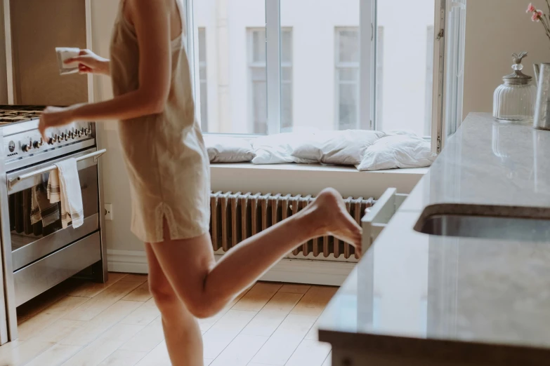 a woman standing in a kitchen next to a stove, by Emma Andijewska, pexels contest winner, arabesque, in shorts, waking up, running freely, bare leg