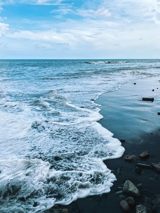 a large body of water sitting on top of a sandy beach, by Robbie Trevino, black sand, blue crashing waves, split near the left, in a beachfront environment