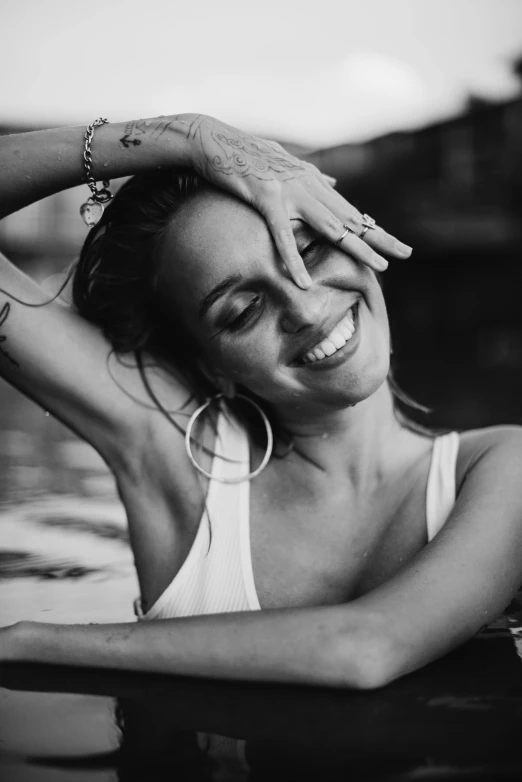 a black and white photo of a woman in the water, disco smile, with tattoos, giorgia meloni, morning golden hour