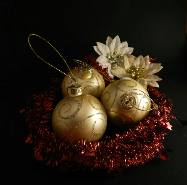 three gold ornaments sitting on top of a red tinsel, a still life, pixabay, process art, with a black background, intricate ornament halo, tribbles, bouquet