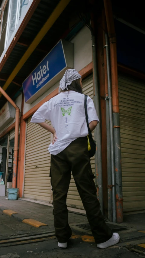 a man standing on a sidewalk in front of a building, an album cover, inspired by Gang Hui-an, pexels contest winner, wearing cargo pants, butterfly, back view also, white t-shirt