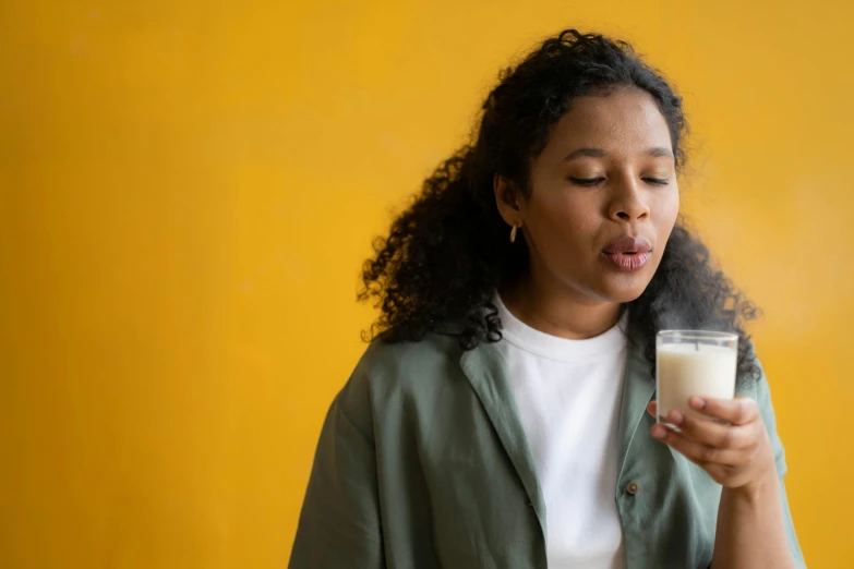 a woman holding a glass of milk in front of her face, trending on pexels, aida muluneh, on a yellow canva, profile image, focus on full - body