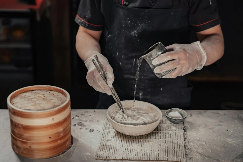 a person pouring something into a bowl on a table, a portrait, inspired by Kanō Naizen, trending on pexels, flour dust, people at work, tanjiro kamado, grey