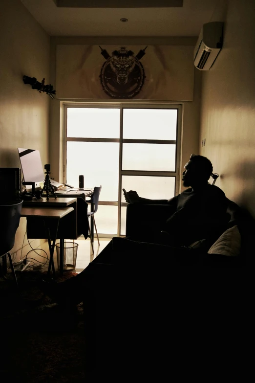 a man sitting in a chair in a dark room, studying in a brightly lit room, lone silhouette in the distance, imgur, sitting in rural living room