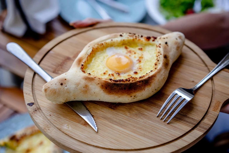 a close up of a plate of food with a fork and knife, inspired by Géza Dósa, hurufiyya, head is an egg, calzone zone, wooden, volcanic