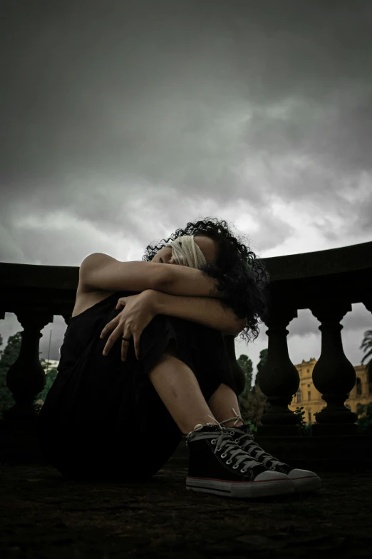 a woman sitting on the ground with her head in her hands, by Lucia Peka, pexels contest winner, romanticism, goth aesthetic, cloudy skies, in balcony of palace, hugging her knees