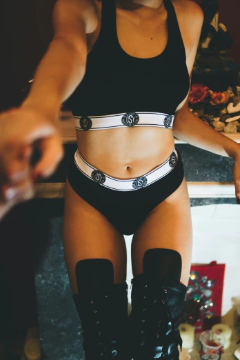 a woman standing in a kitchen next to a counter, by Robbie Trevino, unsplash, renaissance, intricate wet latex suspenders, ying and yang, cute rave outfit, white belt