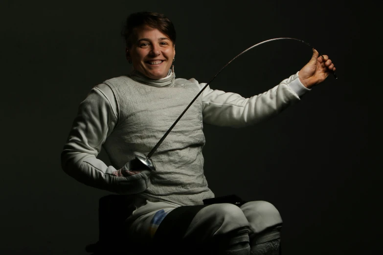 a man sitting on top of a chair holding a sword, fencer, while smiling for a photograph, lachlan bailey, foil