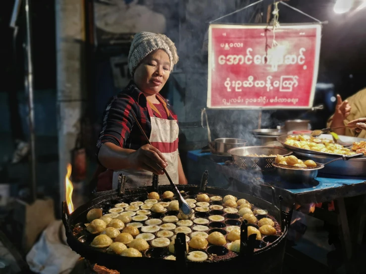 a woman standing in front of a grill filled with food, hurufiyya, nuttavut baiphowongse, square, unsplash photo contest winner, dumplings on a plate