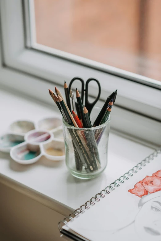 a cup filled with pencils sitting on top of a window sill, visual art, crayons and watercolor sketch, white wall coloured workshop, product display photograph, glass paint