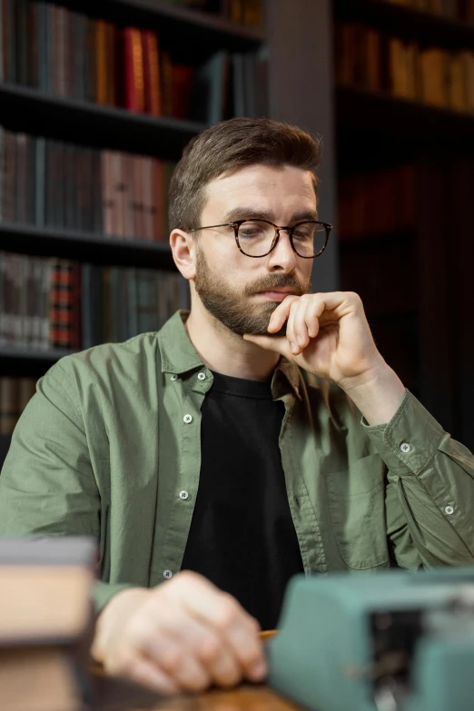 a man sitting at a table with a typewriter, by Adam Marczyński, shutterstock, realism, wearing square glasses, wearing dark green bomber jacket, in a library, looking serious