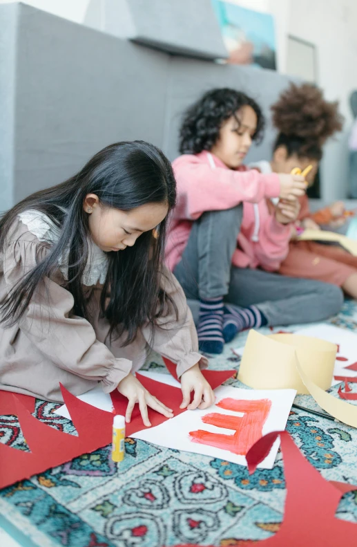 a group of children sitting on the floor working on crafts, pexels contest winner, process art, young asian girl, cut and paste, wearing red clothes, geometry