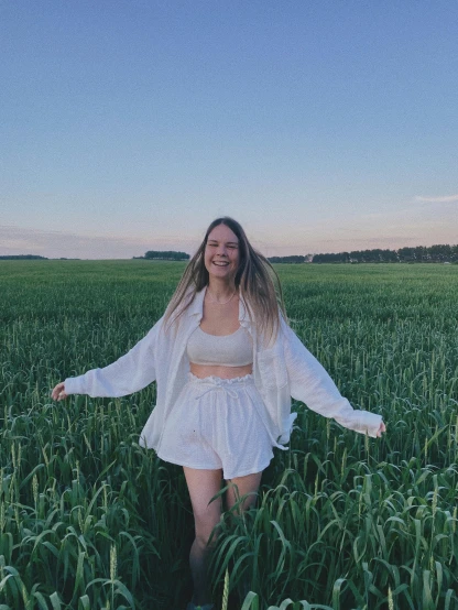 a woman standing in a field of tall grass, an album cover, pexels contest winner, happening, croptop and shorts, greta thunberg smiling, wearing white robes!, photo taken at night