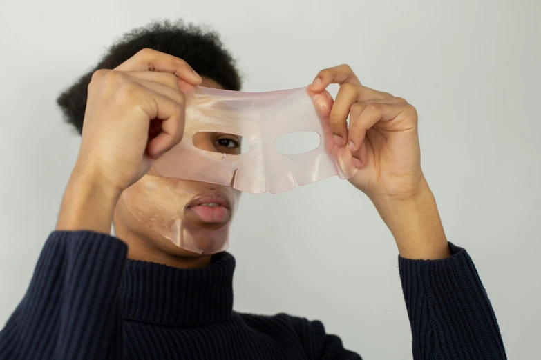 a woman putting a mask on her face, by Nina Hamnett, silicone skin, wearing translucent sheet, on clear background, middle shot