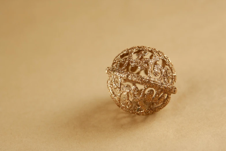 a close up of a ring on a table, a stipple, by Ruth Simpson, unsplash, arabesque, ball, beige and gold tones, 3 d print, detailed product shot