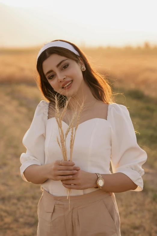 a woman standing in a field holding a bunch of grass, an album cover, inspired by Altoon Sultan, trending on pexels, a beautiful woman in white, puff sleeves, square, young middle eastern woman