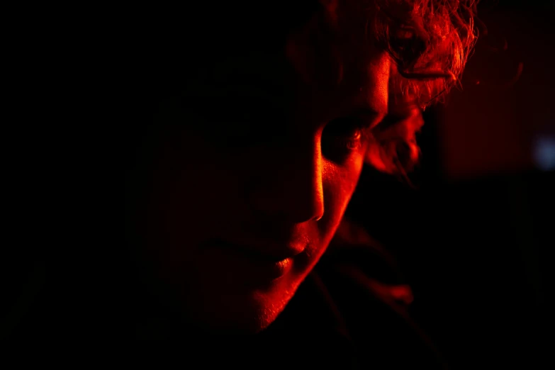 a close up of a person in a dark room, an album cover, inspired by Lasar Segall, pexels, at gentle dawn red light, teenage boy, julia garner, red monochrome