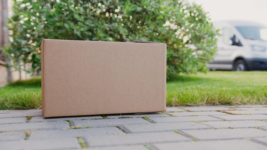 a cardboard box sitting on the ground in front of a van, pexels contest winner, with a lush grass lawn, no - text no - logo, background image, paved