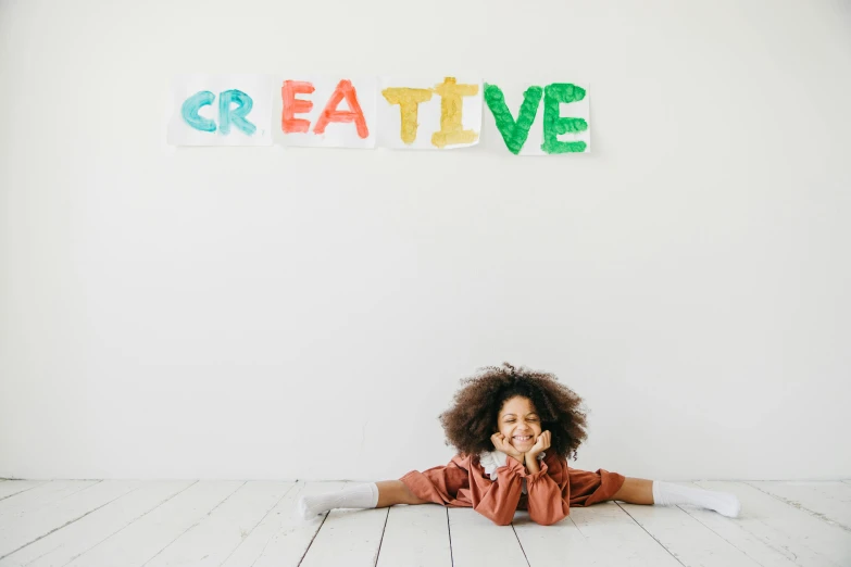 a little girl sitting on the floor in front of a sign that says creative, a child's drawing, pexels contest winner, photo of a black woman, in white room, plain background, background image